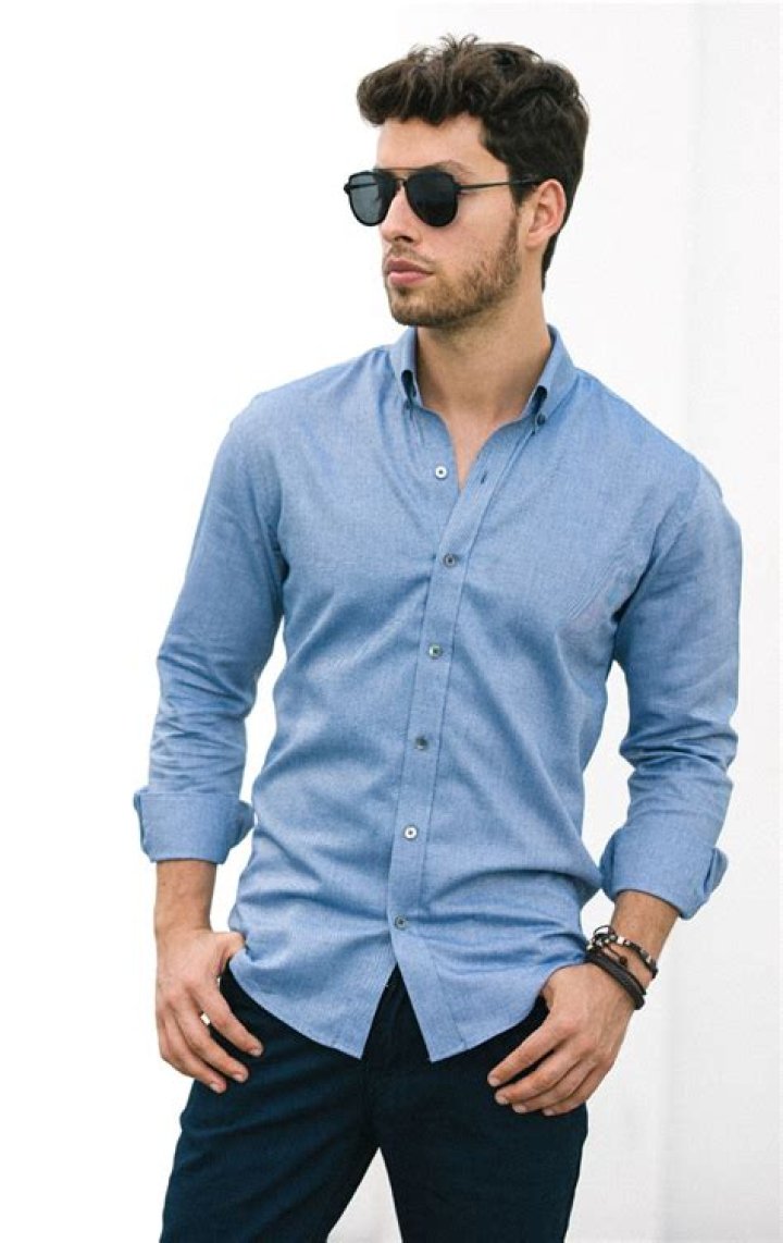 a man wearing a blue shirt with a necklace on his neck is looking at